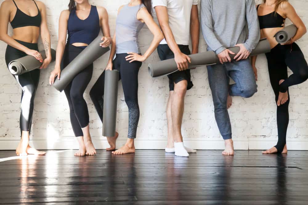 Group of sporty people holding mats as they stand against the brick wall.