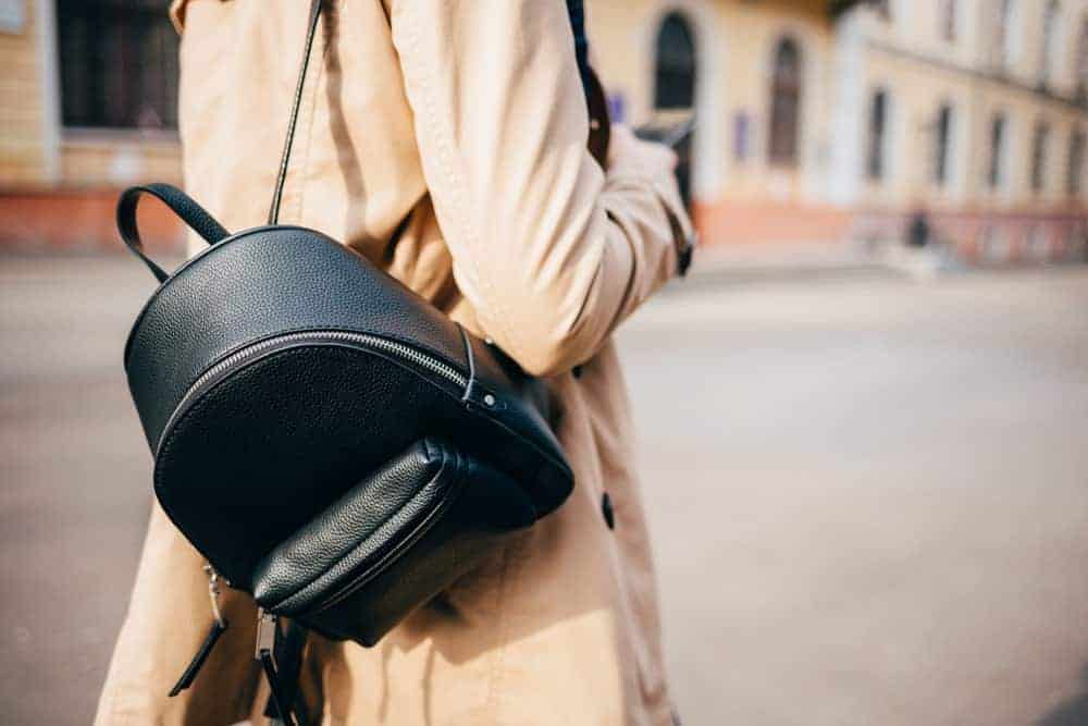 Woman in beige coat with black backpack.
