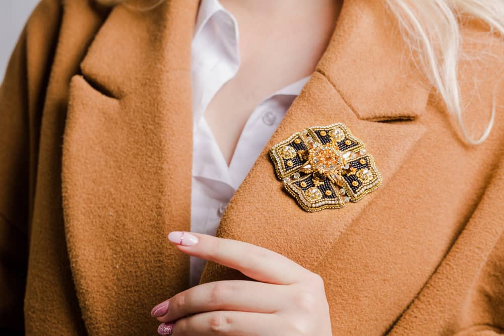 Woman in beige coat with brooch.