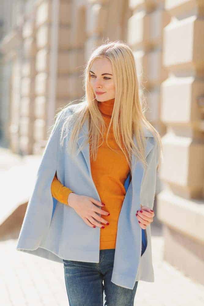 Woman wearing a blue cape sweater over an orange turtleneck long sleeves.