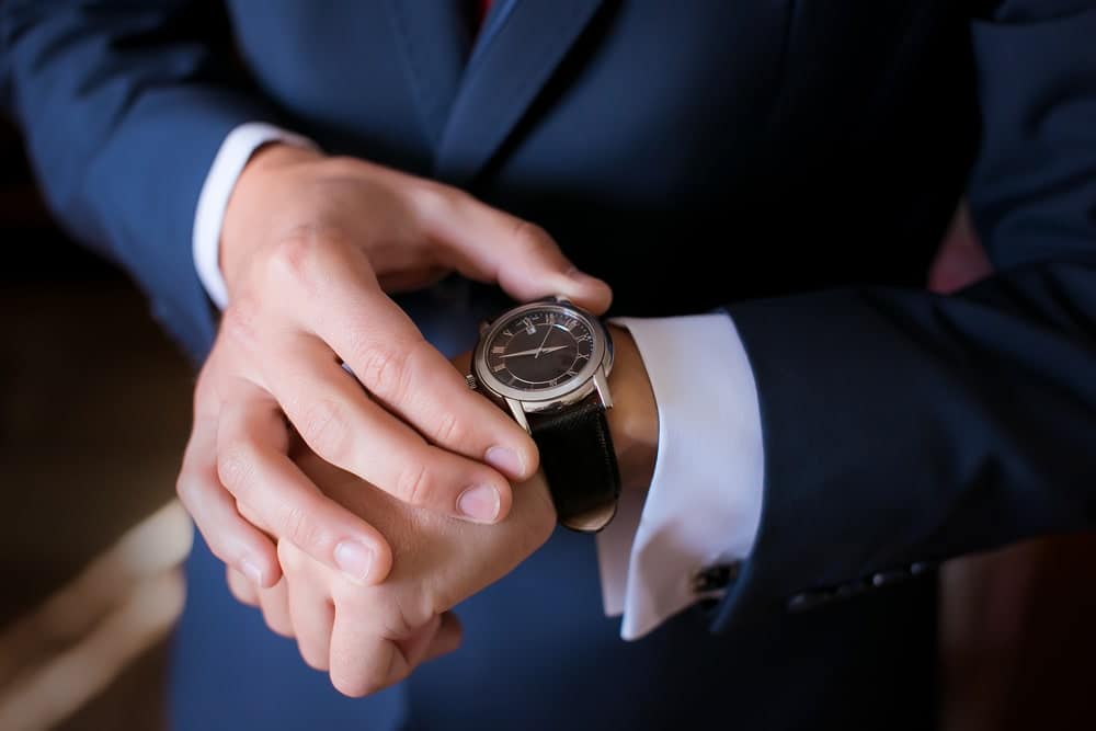Groom in a wedding suit looking at his dress watch.