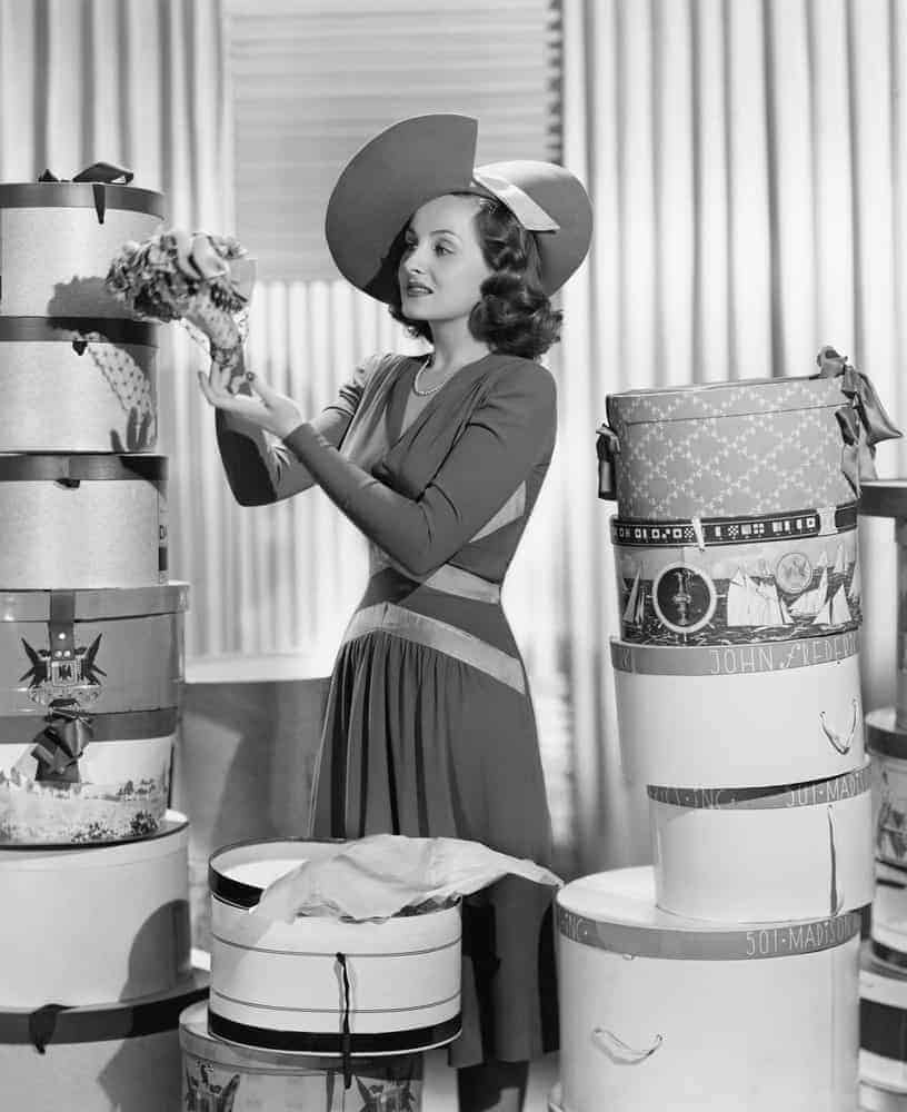 Women bordered by piles of hat boxes.