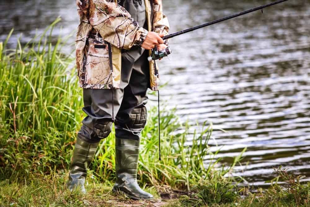 A man in hip boots fishing on the river bank.