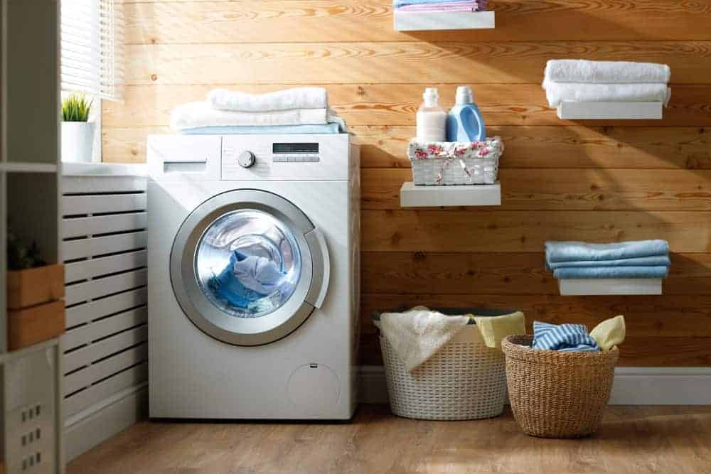 Laundry room with front load washing machine, floating white shelves, and wicker hampers.