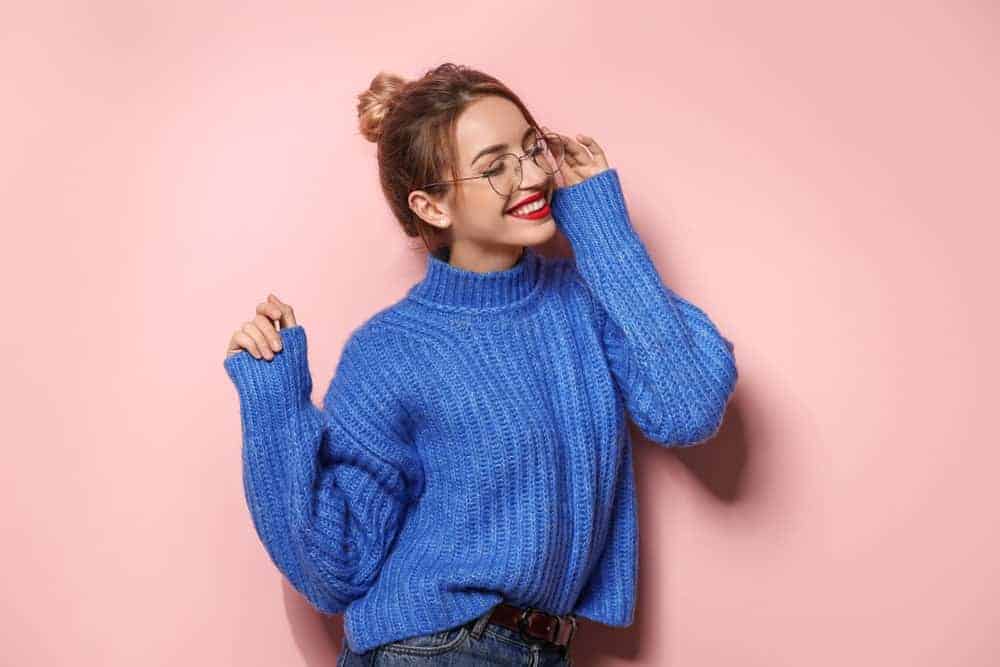Woman in a high bun wearing a blue raglan sweater.