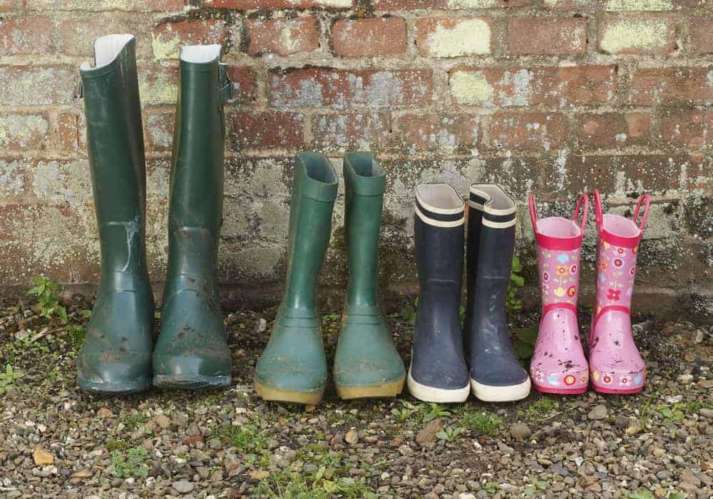 A row of rain boots against an old brick wall.