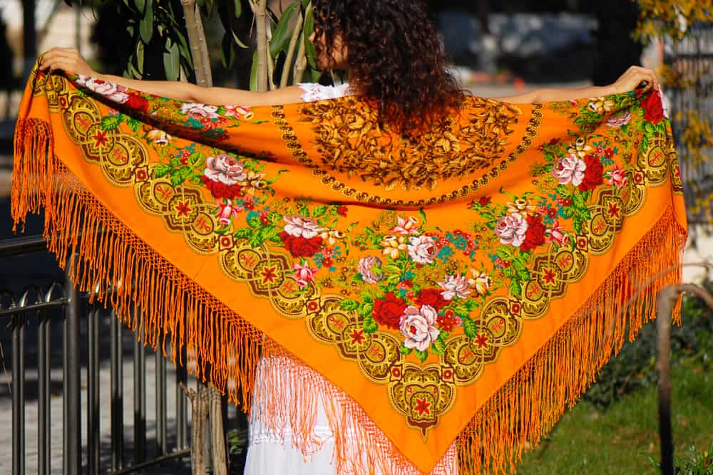 Back profile of a girl holding a tasseled shawl.