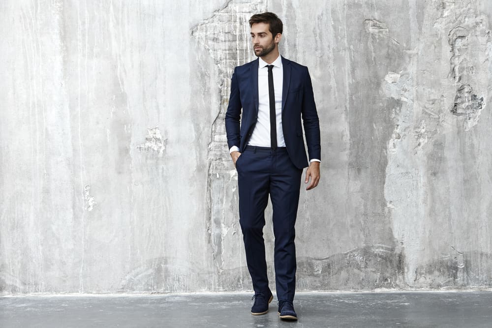 Man in suit poses against the concrete wall.