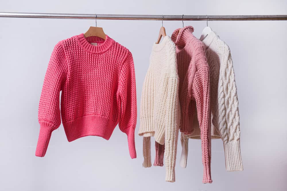 Four knitted sweaters hanging on a rod.