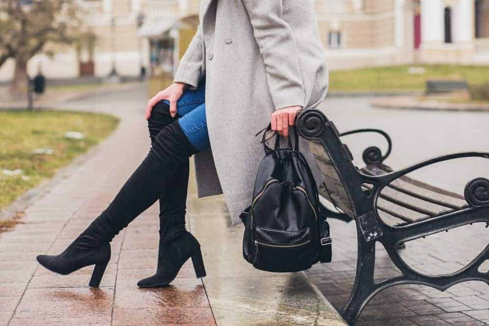 A woman sitting on a bench with her thigh-high boots.