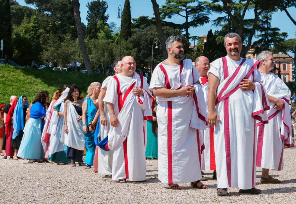 Men wearing white tunica with purple-red strips and toga during the parade.