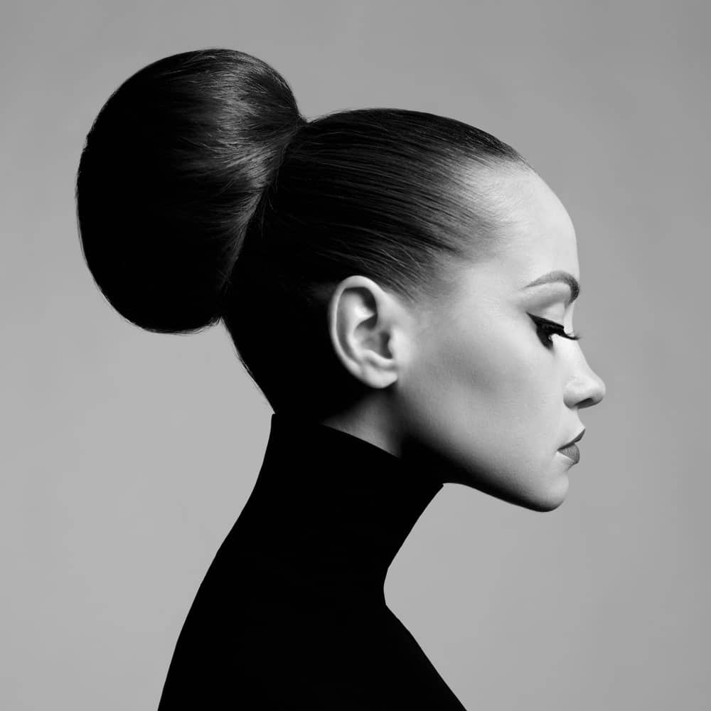 Woman in a bun hairstyle wearing a black turtleneck sweater.