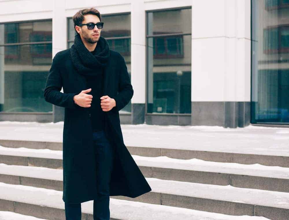 A man wearing a long coat and a pair of sunglasses.