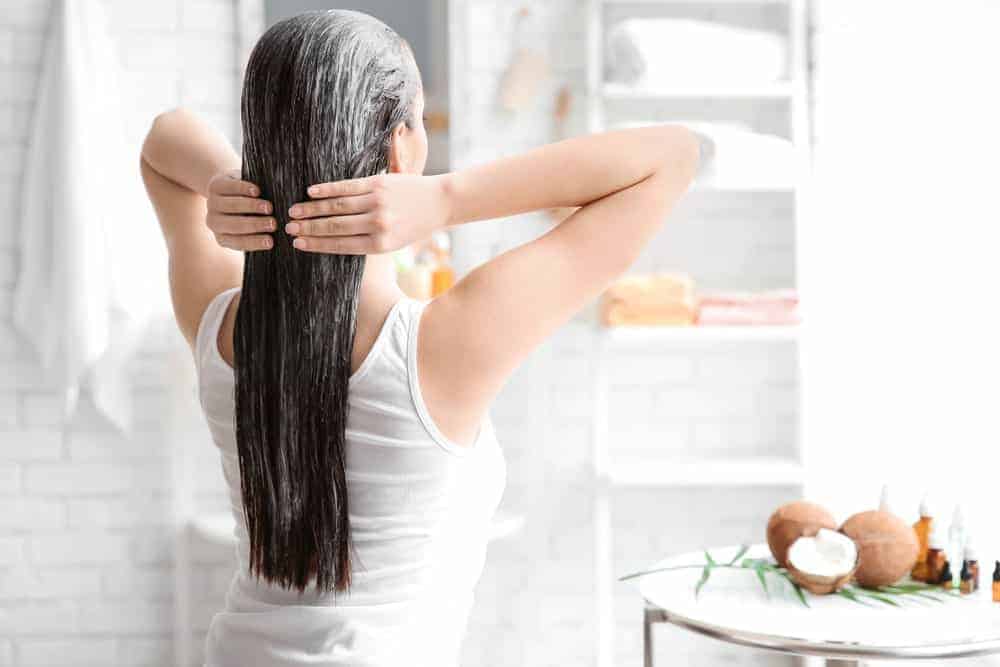 A woman oiling her hair in the bathroom.