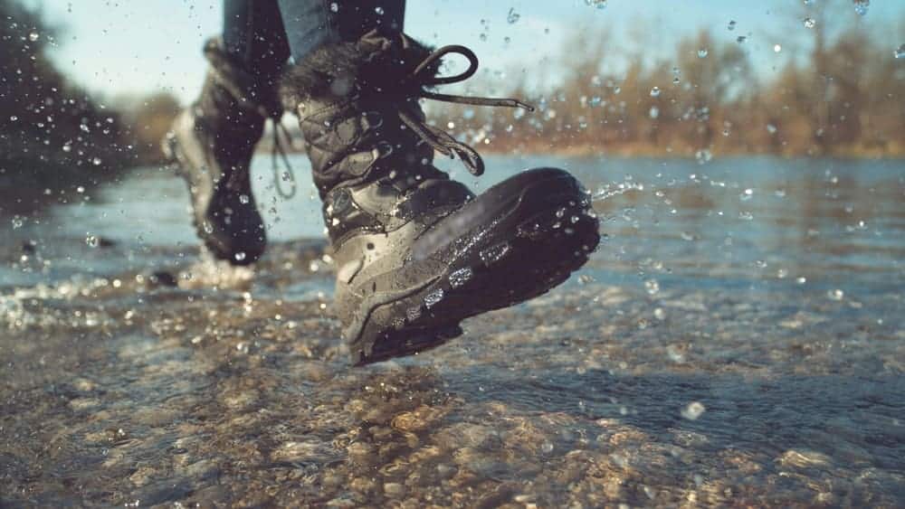 A woman in boots walking on a stream.