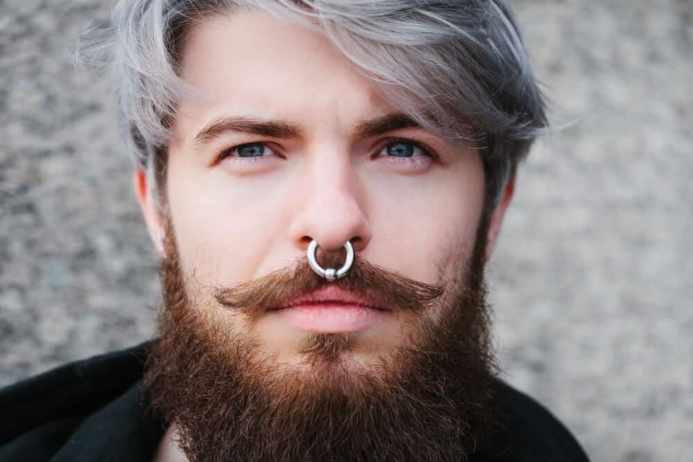 A close look at a bearded man with a nose ring.