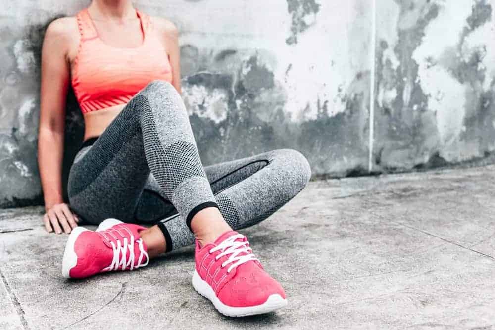 Woman wearing sportswear, sitting on the ground, leaning on the wall.
