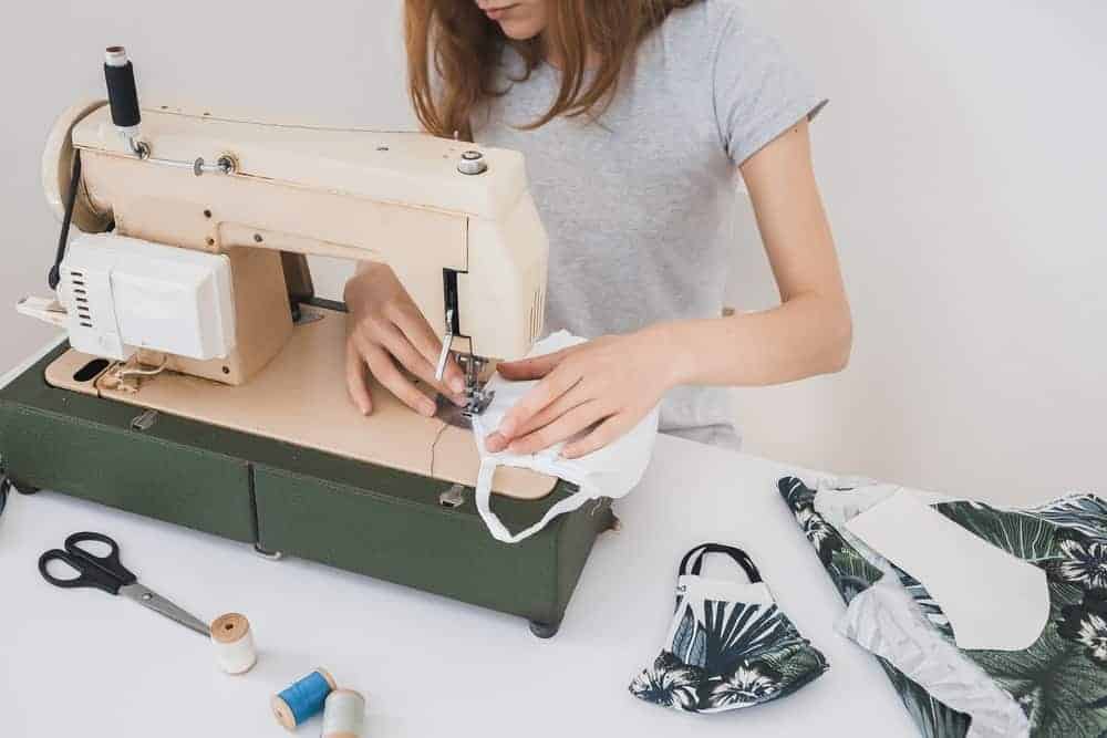 A woman making face masks with the use of a sewing machine on a desk.