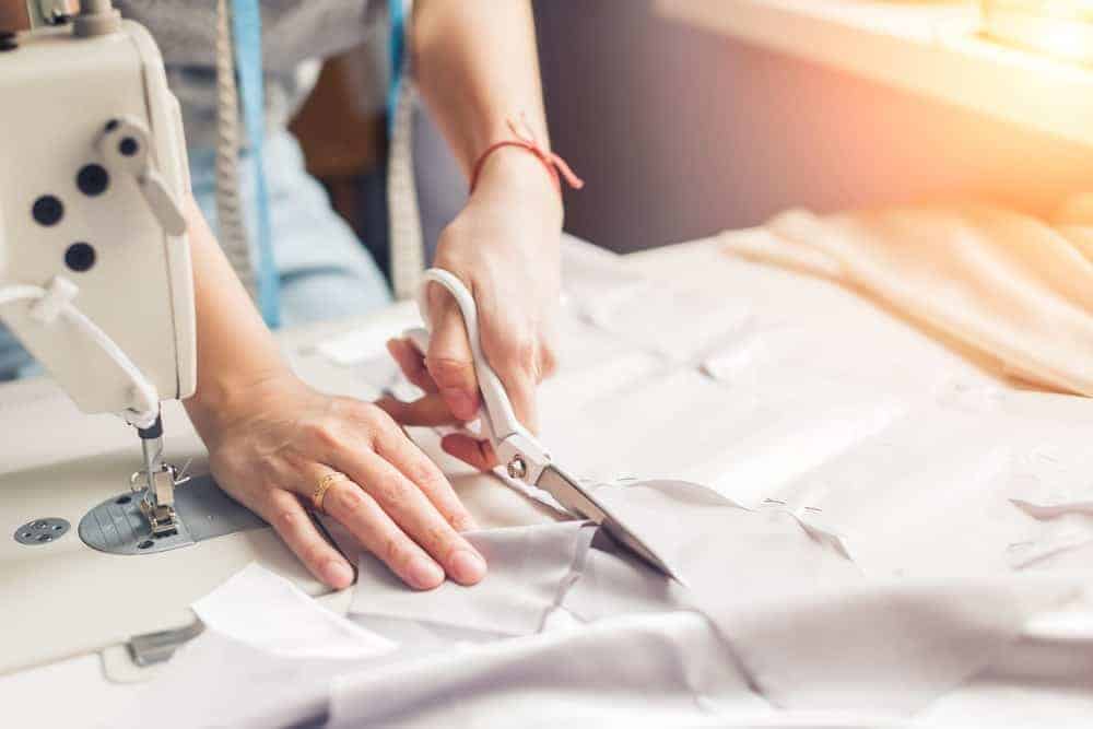 A woman cutting up a white piece of cloth to be used for sewing.