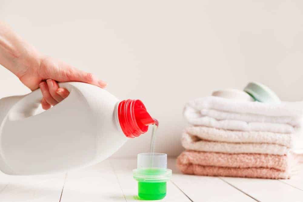 A bottle of liquid detergent being poured onto a measuring cup.