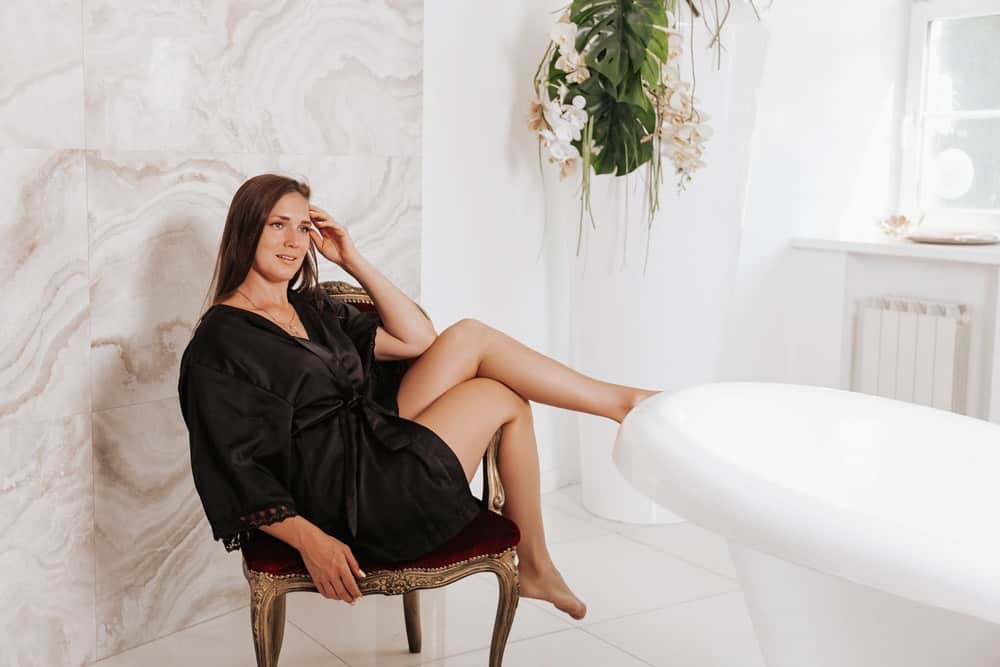 A woman sitting by the bathtub wearing black silk negligee.