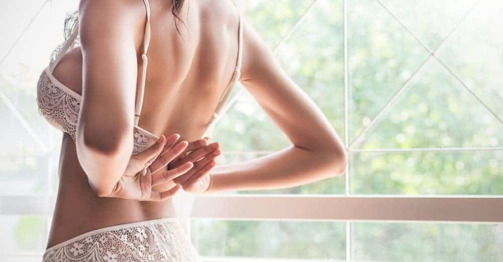 A woman putting on a white lace bra.