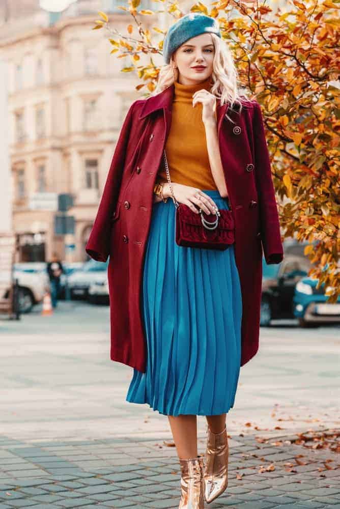 A woman wearing matching items like her bag and jacket as well as her skirt and beret.