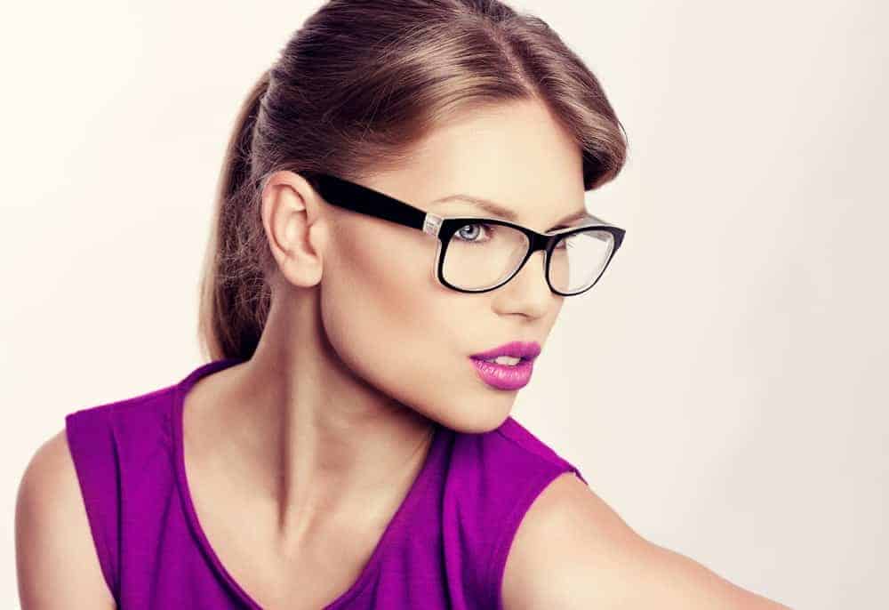 A woman wearing a pair of glasses with her makeup that matches her blouse.