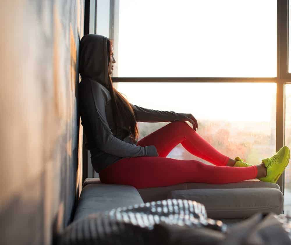 A woman wearing a pair of bright leggings relaxing by the window.