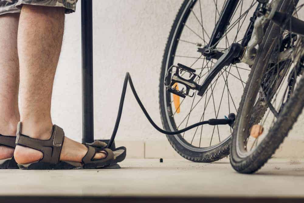 A man wearing a pair of sandals inflating his bike.