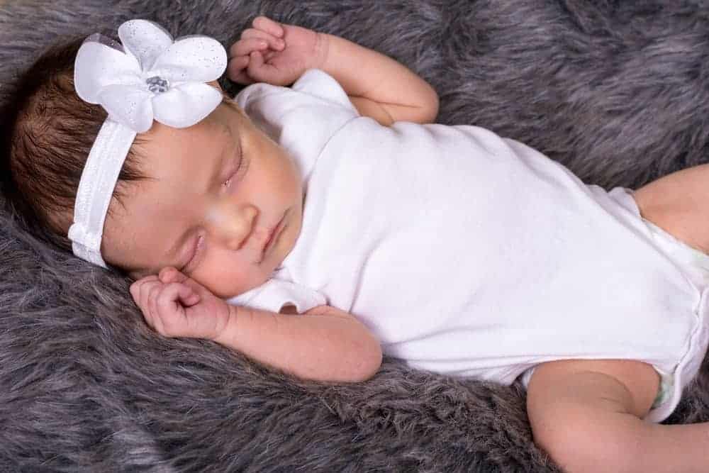 A baby wearing a white onesie on a shag carpet.