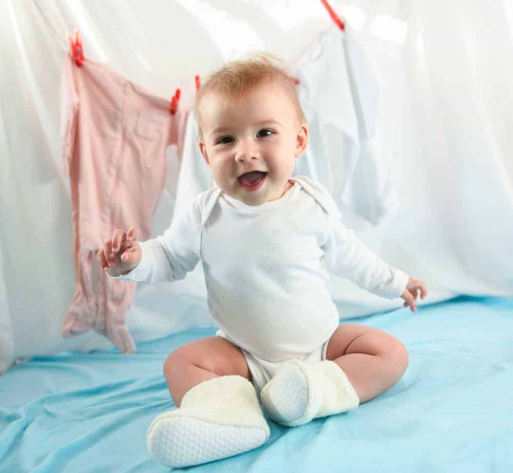 A baby sitting up wearing a white onesie.