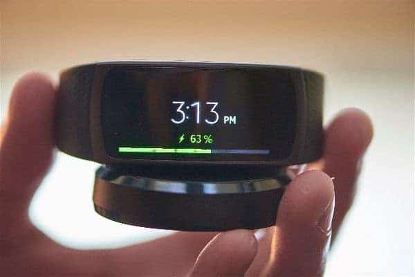 A close look at the Samsung Gear Fit 2 Smartwatch that is charging to show the size in proximity to hand.