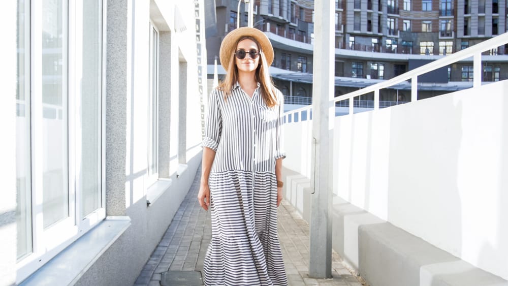 Woman in sunglasses and long shirtwaist dress walking on street.