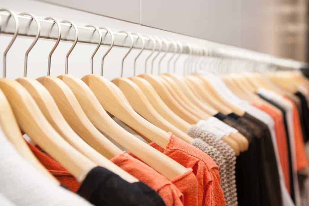 A row of clothes in wooden clothes hangers on display at a store.