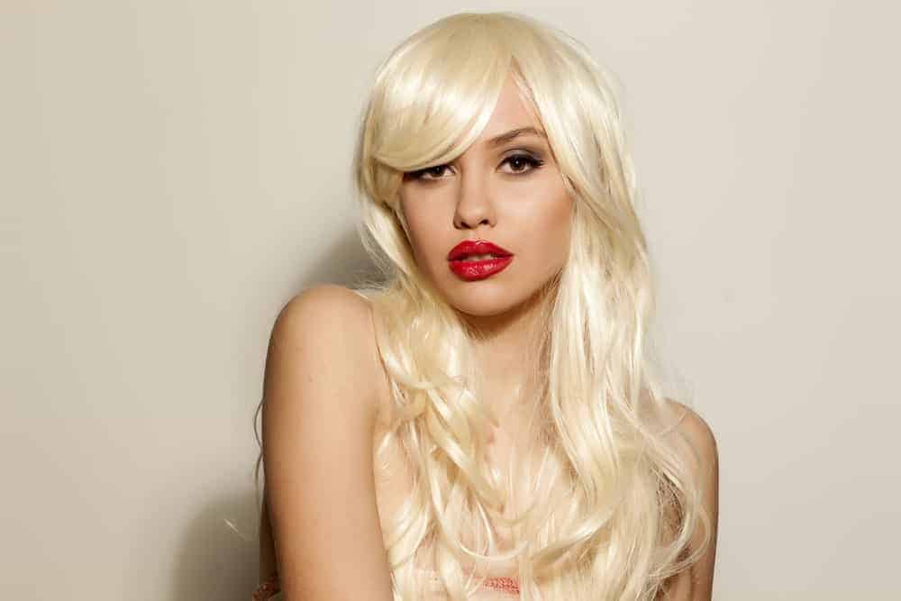 A woman wearing a long blonde wig with bangs.