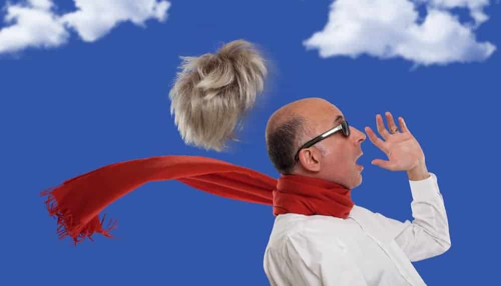 A man with his toupee blown away by the wind.