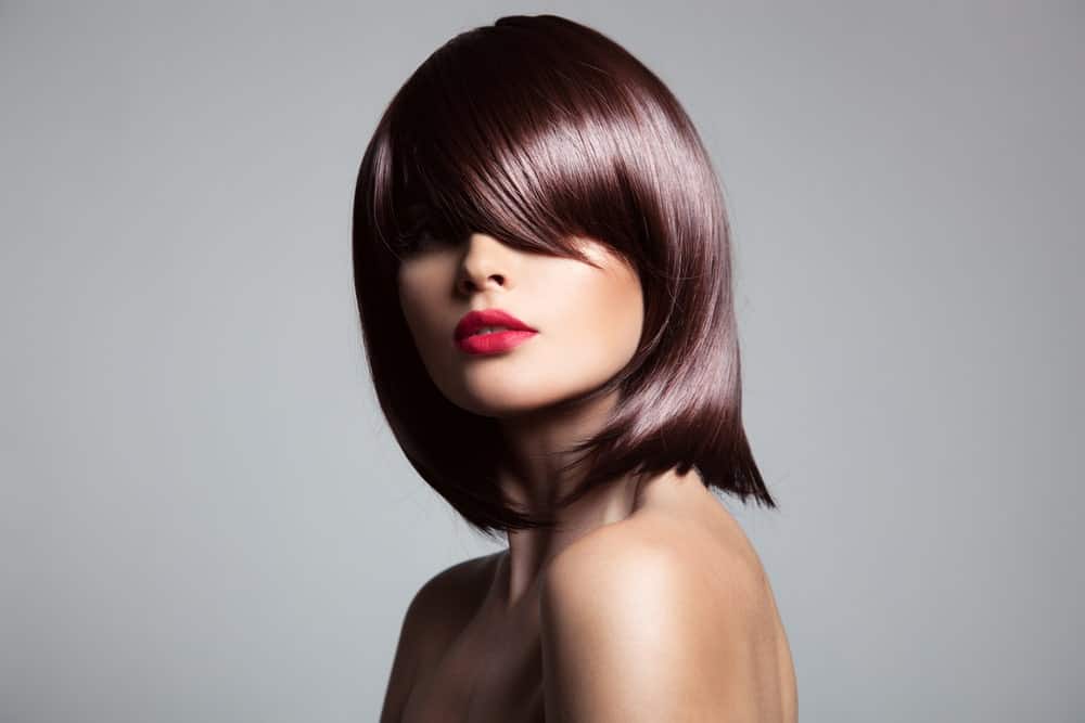 A woman wearing a dark brown silky wig with bangs.