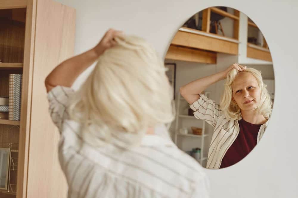 An old woman taking her wig off in front of the mirror.