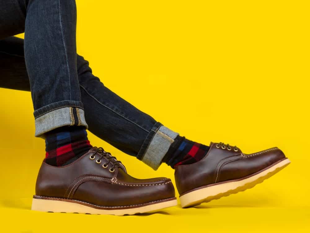 This is a close look at a man wearing a pair of brown leather derby shoes and jeans.