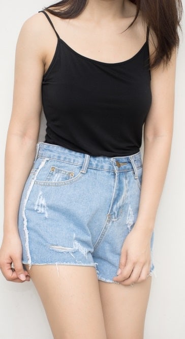 A woman wearing a pair of denim shorts with her camisole top.