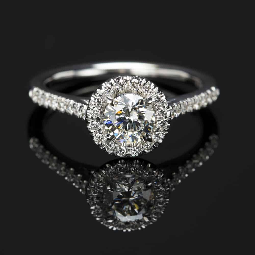 This is a close look at a halo diamond ring on a dark reflective surface.