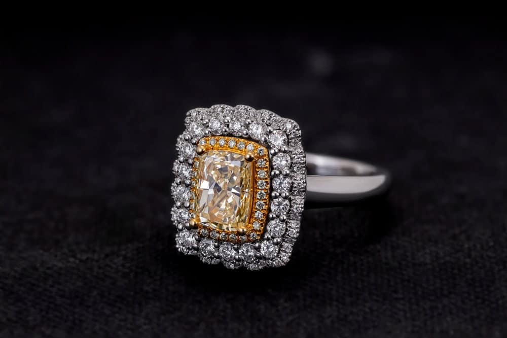 This is a cushion cut ring with diamonds on a dark surface.