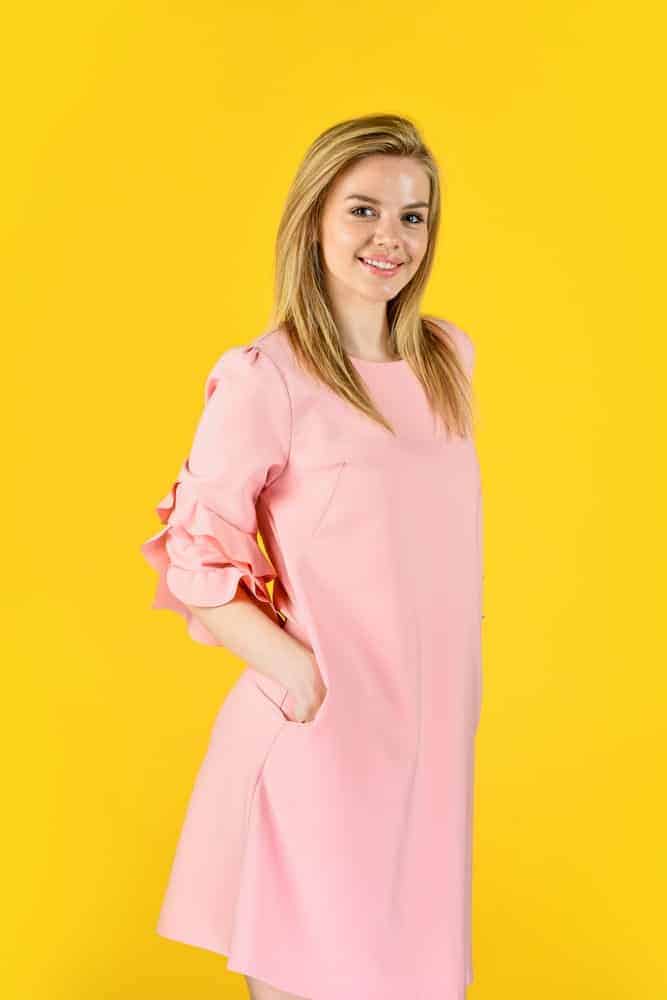 A close at a woman wearing a pink dress that has frill sleeves.