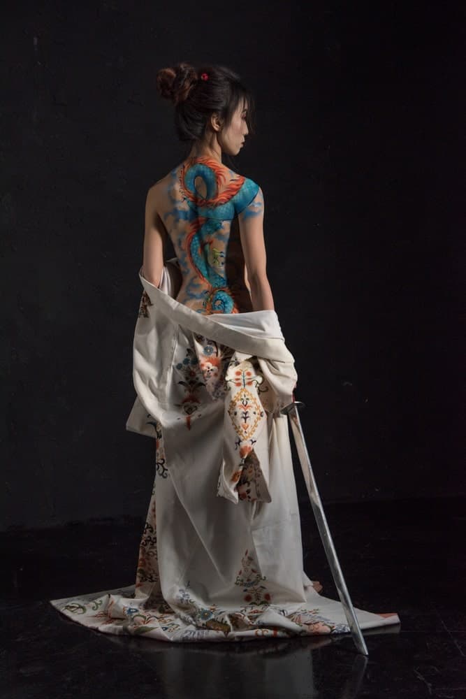 This is a look at a woman holding a katana with a dragon tattoo on her back.