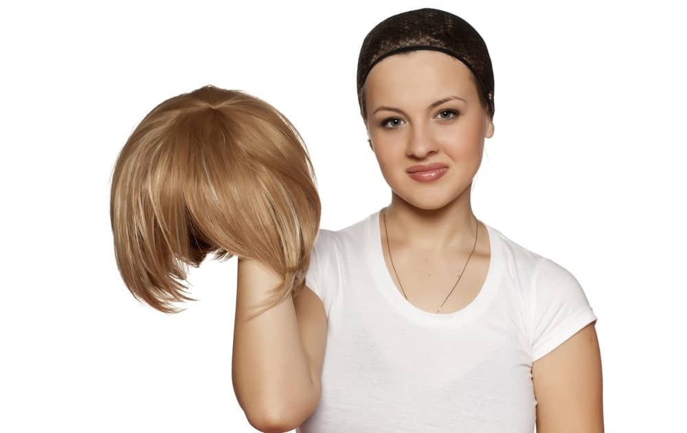 A woman wearing a wig cap holding a wig.