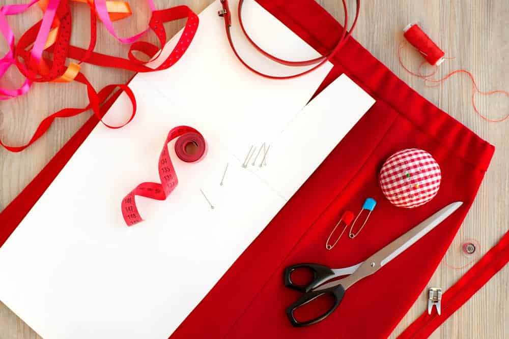 Red skirt topped with a tape measure, tailoring scissors, pin cushion, and safety pins.