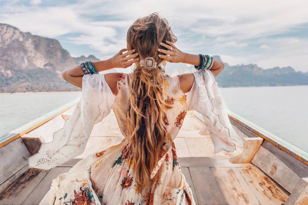 Woman in a loose dress standing near the edge of a boat.