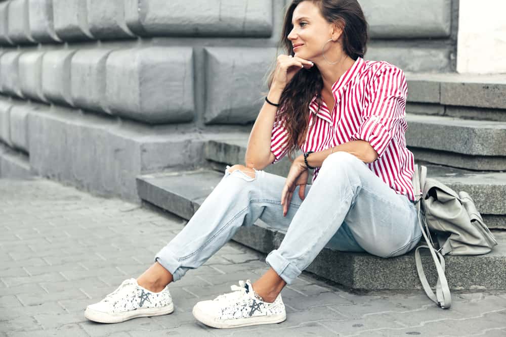 Woman wearing ripped boyfriend jeans, red striped shirt, sneakers and backpack.