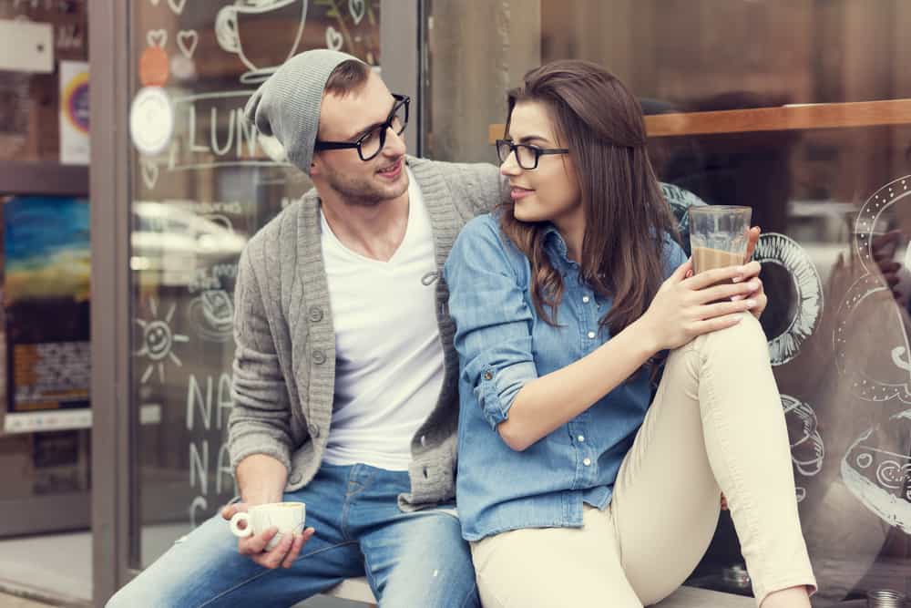 A couple in geeky style outfits enjoying their cups of coffee.
